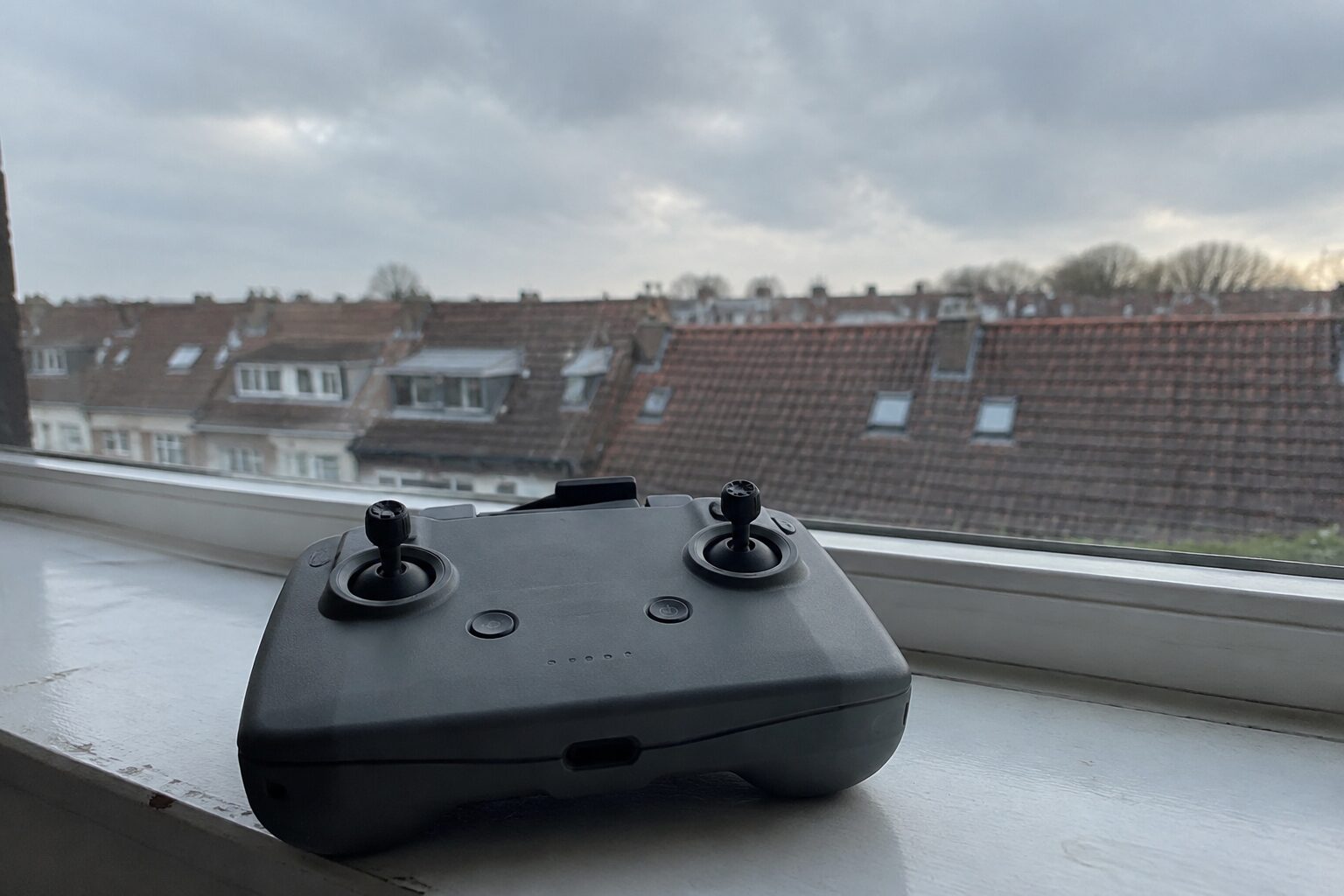 Controller op een vensterbank met bewolkte lucht en daken erachter