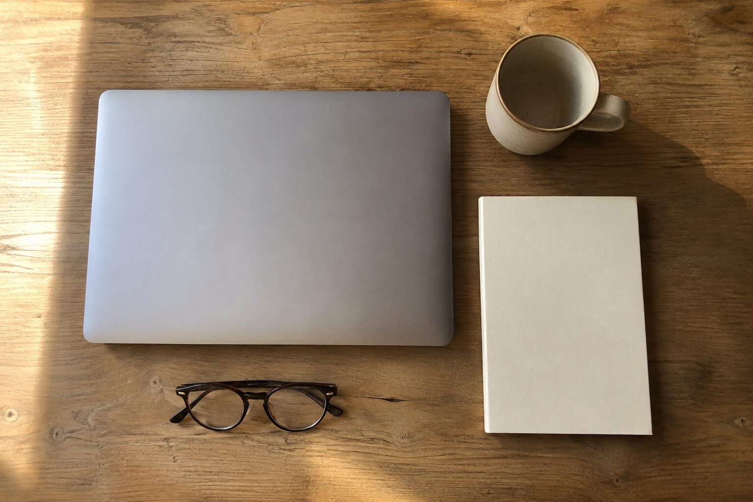 Werkplek van bovenaf met laptop, mok, notitieboek en bril
