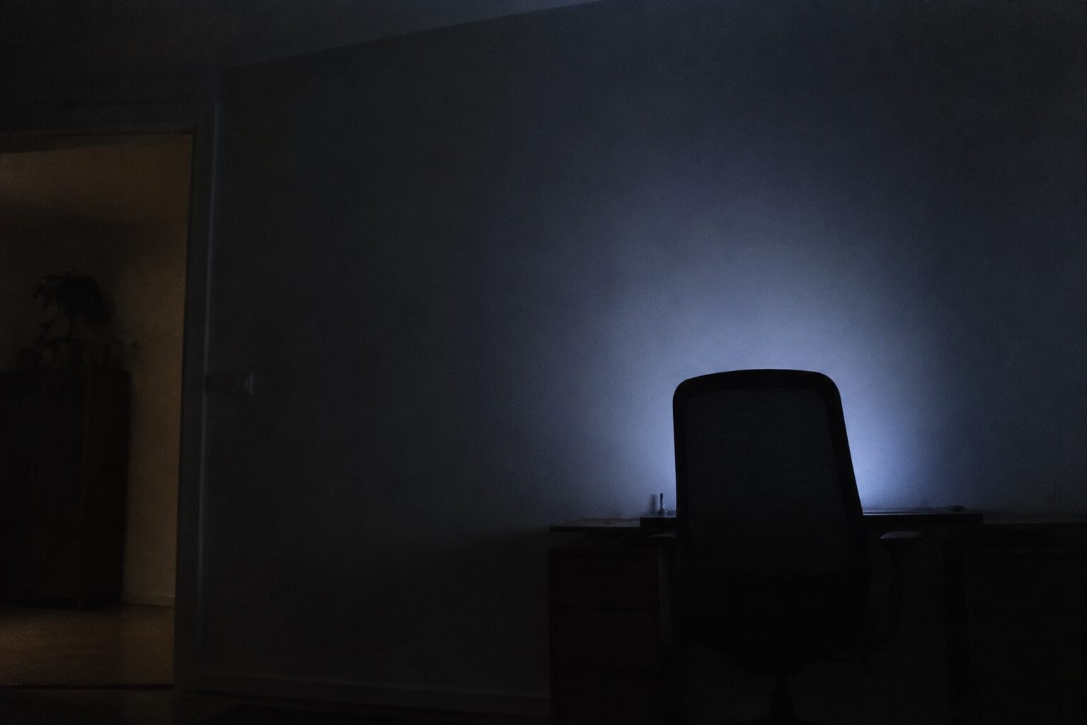 Donkere kamer met alleen schermlicht op de muur en het silhouet van een stoel